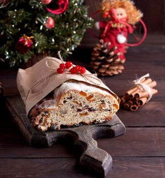 Stollen a traditional European cake with nuts and candied fruit, is dusted with icing sugar on a brown wooden board