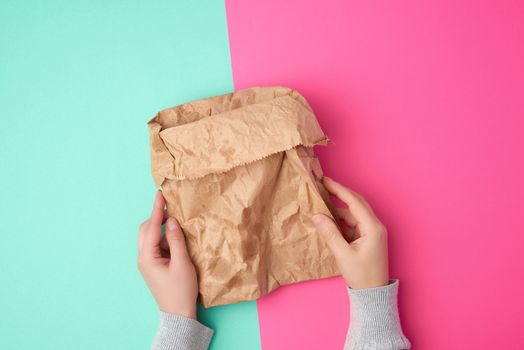 two female hand holding open brown paper bag for food packaging with greasy stains on a green pink background, concept of rejection of plastic bags to save the environment