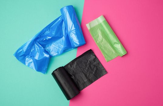 three rolled up rolls with plastic garbage bags on a green pink background, top view