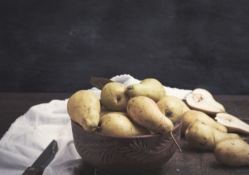 fresh ripe green pears in a brown clay bowl on a table, close up