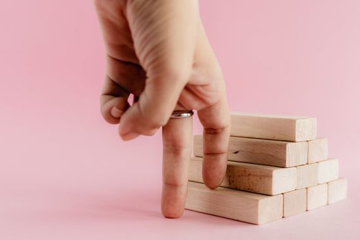 Fingers moving step up the wooden toy staircase on pink background for step to goal success concept