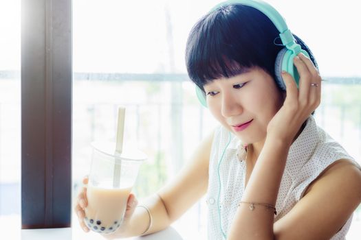 Asian woman wearing headphones and holding a plastic cup of bubble tea with blurred background for drinks, beverage and stay at home concept