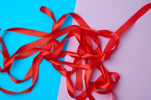 lot of red satin ribbon on a colored background, preparation for gift wrapping, top view