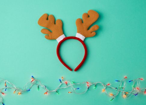 burning christmas garland on a white wire with colorful lights and carnival deer head mask on a green background, copy space