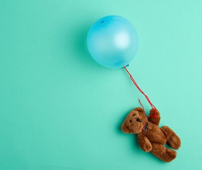 little brown teddy bear holding a pink inflated balloon on a rope on a green background
