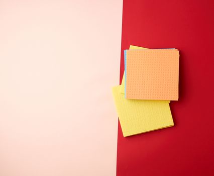 multi-colored square dishwashing sponges on a red-beige background, top view, flat lay