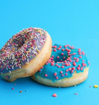 two round baked donut with colored sugar sprinkles and with blue sugar icing on a blue background