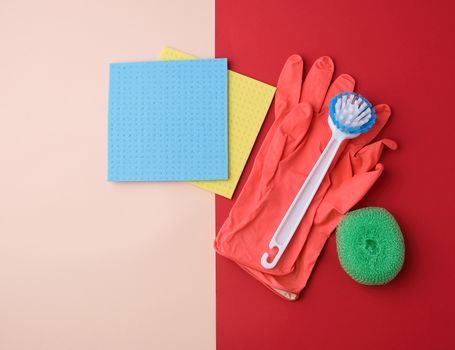 items for home cleaning: red rubber gloves, brush, multi-colored sponges for dusting on a colored background, top view, flat lay