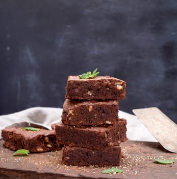 stack of baked square pieces of chocolate brownie pie with walnuts, close up