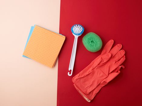 items for home cleaning: red rubber gloves, brush, multi-colored sponges for dusting on a colored background, top view, flat lay