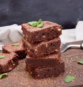 stack of baked square pieces of chocolate brownie pie with walnuts, close up