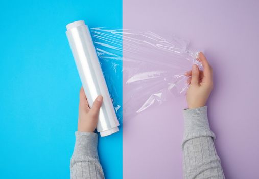 two hands hold a large roll of wound white transparent film for wrapping food, top view