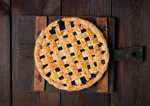 whole baked round black currant cake on brown wooden background, top view