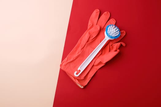 white brush and pink rubber gloves for cleaning the house on a red-beige background, top view, flat lay