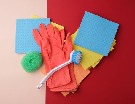 items for home cleaning: red rubber gloves, brush, multi-colored sponges for dusting on a colored background, top view, flat lay
