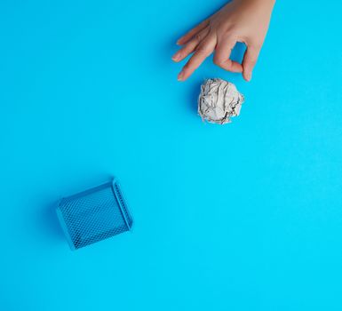 hand pushed a ball of crumpled gray paper into a metal wastebasket, concept of waste recycling and environmental pollution