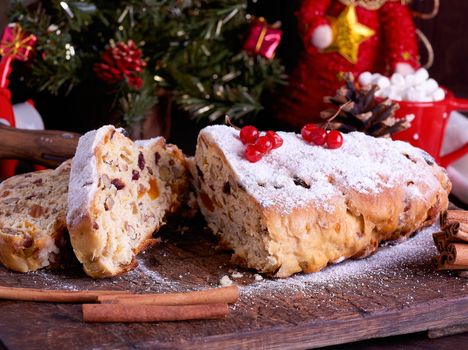 Stollen a traditional European cake with nuts and candied fruit, is dusted with icing sugar and cut into pieces on a brown wooden board