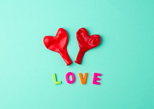 two red rubber balloons blow away in the shape of a heart on a green background