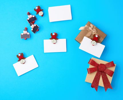 boxes with red bows, blank white business cards and decorative clothespins on a blue background, top view