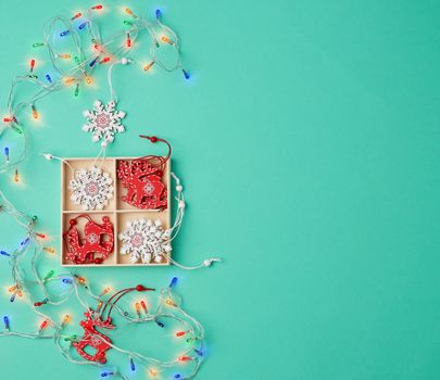 burning christmas garland on a white wire with colorful lights and box with wooden toys for the Christmas tree on a green background, copy space