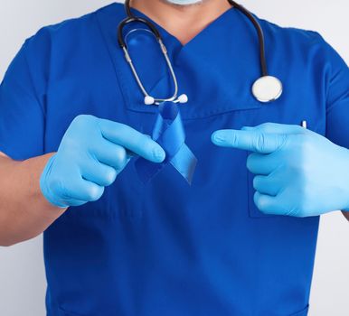 doctor in blue uniform and sterile latex gloves holds a dark blue ribbon, concept of timely research and disease prevention colon malignancies, chronic fatigue syndrome, tuberous sclerosis