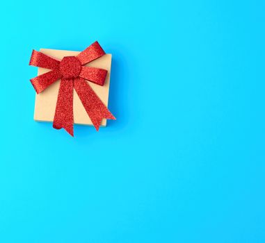 closed brown gift box with a red shiny bow on a blue background, top view, copy space