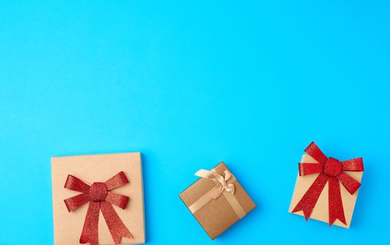 three closed square gift boxes with bows on a blue background, top view, place for text