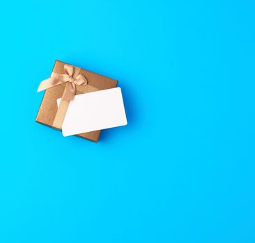 closed brown gift box with bow and empty paper business card on a blue background, top view