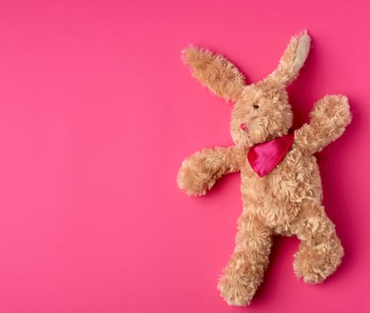 toy brown plush hare lies on a pink background, copy space
