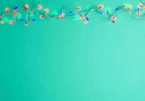burning christmas garland on a white wire with colorful lights on a green background, copy space