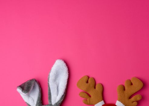 protruding ears of a rabbit mask and brown deer horns on a pink background, Christmas costumes, copy space