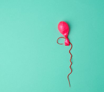 deflated rubber pink balloon and red rope on a green background, copy space