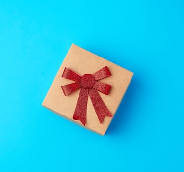 square gift box with a red bow on a blue background, top view, festive backdrop