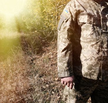 fragment of the hand of a Ukrainian soldier in military camouflage uniform with a patch of the Ukrainian flag, close up