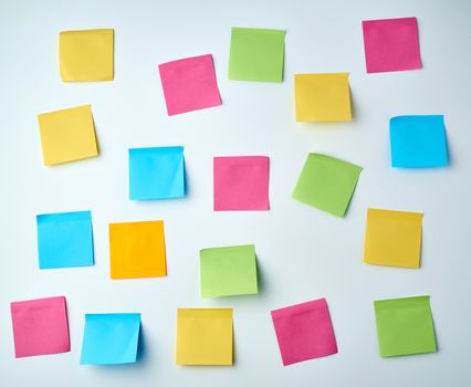 lot of blank square paper multicolored stickers on a white wall, close up