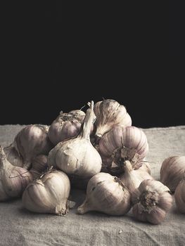 heap of raw unpeeled garlic on a vintage gray linen napkin, dark background