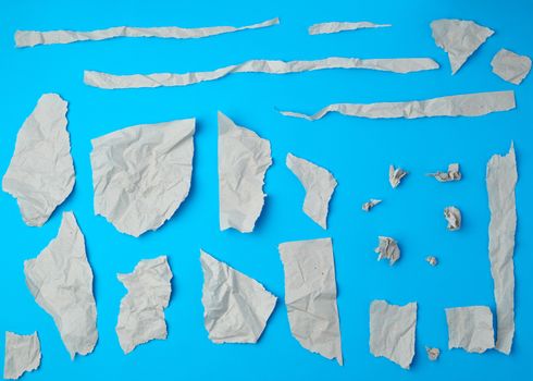 set of various pieces of torn gray crumpled paper on a blue background, close up