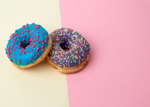 round baked donut with colored sugar sprinkles and with blue sugar glaze on a pink-yellow background, top view