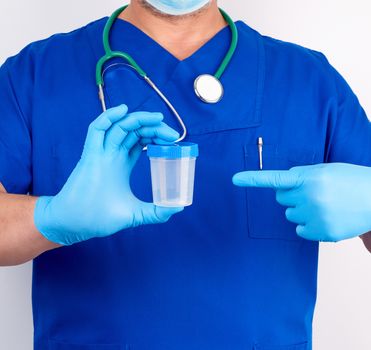 doctor in blue uniform and latex gloves is holding an empty plastic container for taking urine samples, close up