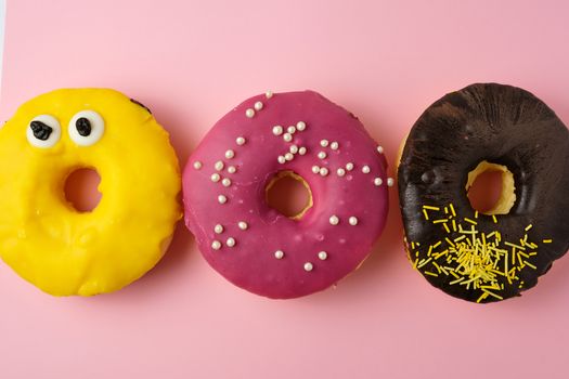 three round different sweet donuts with sprinkles on a yellow background, top view