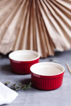 Small glazed ceramic ramekin. Ceramic baking dish. Red baking cup for cupcakes, muffins on a gray and white background