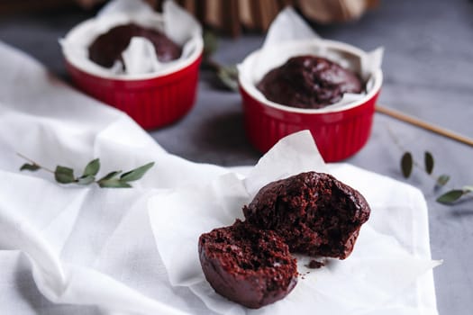 Chocolate muffins in red cups. Small glazed ceramic ramekin with brown cakes on a gray and white background