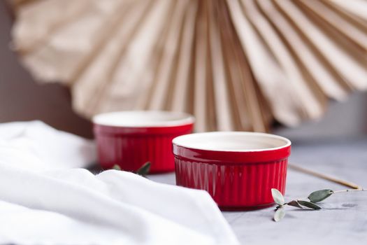 Small glazed ceramic ramekin. Ceramic baking dish. Red baking cup for cupcakes, muffins on a gray and white background