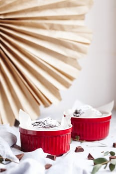 Chocolate muffins in red cups. Small glazed ceramic ramekin with brown cakes on a gray and white background