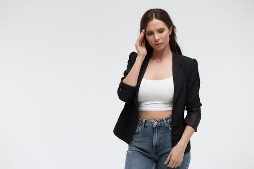 Tired exhausted stressful young female in casual outfit having headache and rubbing temples standing against white background