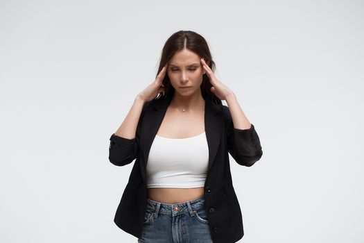 Tired exhausted stressful young female in casual outfit having headache and rubbing temples standing against white background