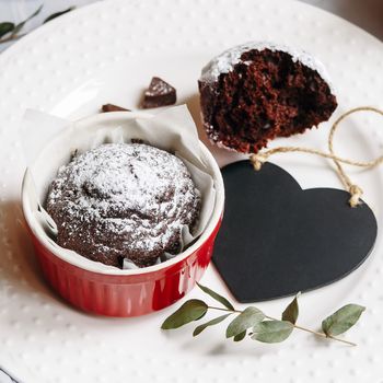 Chocolate muffin in red cup. Mockup valentine black heart copyspace. Small glazed ceramic ramekin with brown cake on a white background