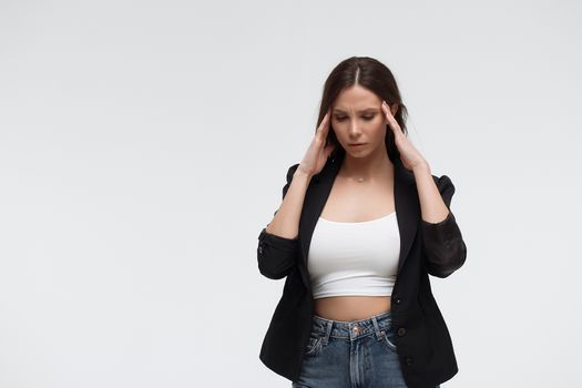 Tired exhausted stressful young female in casual outfit having headache and rubbing temples standing against white background
