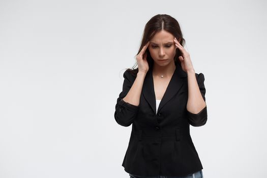Tired exhausted stressful young female in casual outfit having headache and rubbing temples standing against white background