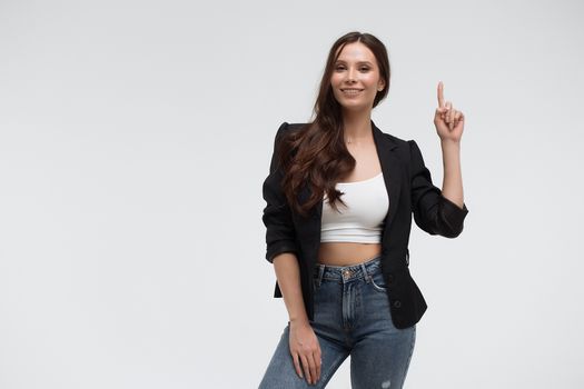 Smiling amazed young brunette in black turtleneck having idea and pointing forefinger up while standing against white background
